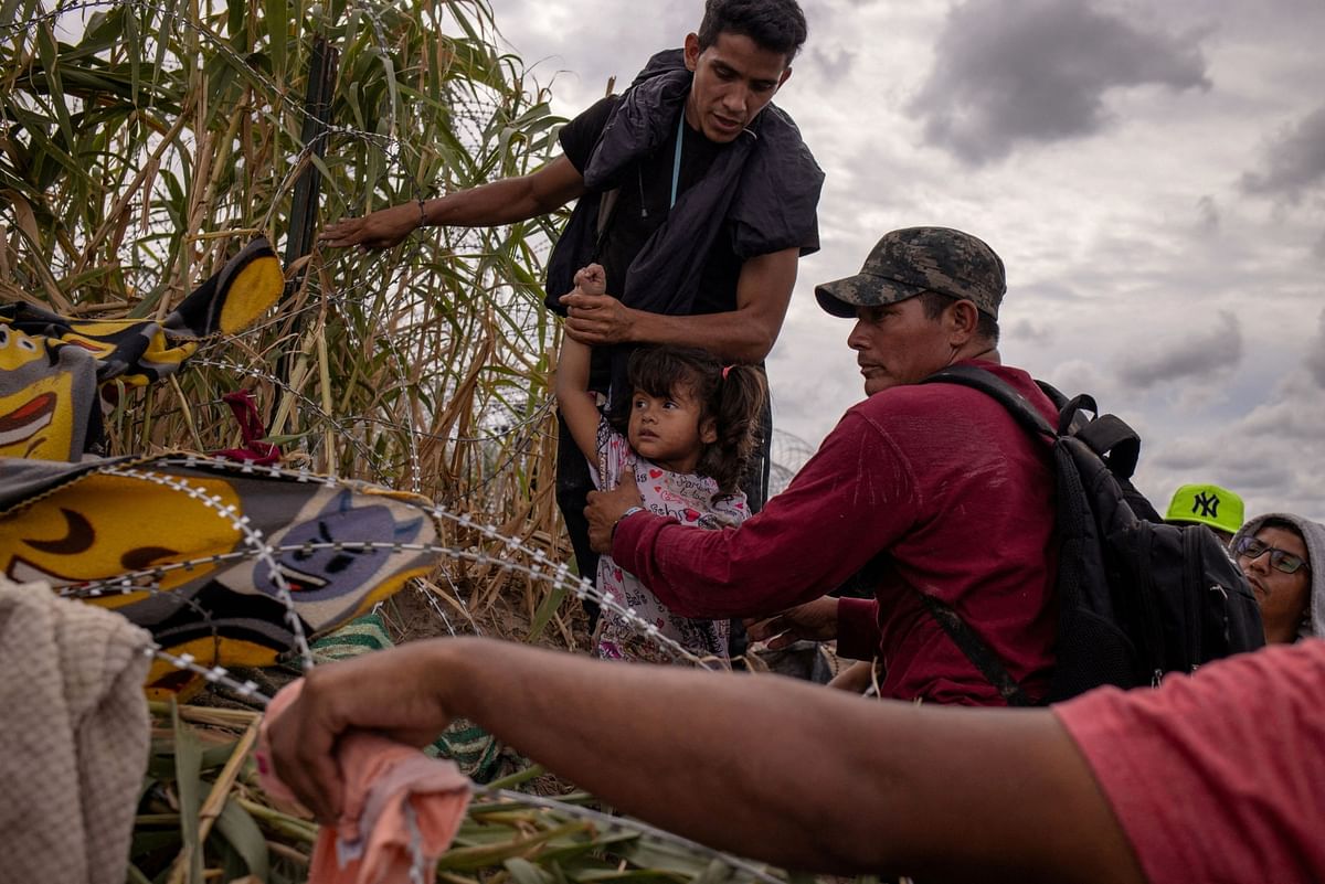 Marina, a four-year-old migrant girl from Venezuela traveling with her mother, is assisted by compatriots as they attempt to navigate past razor wire laden along the banks of the Rio Grande river after wading into the United States from Mexico in Eagle Pass, Texas.