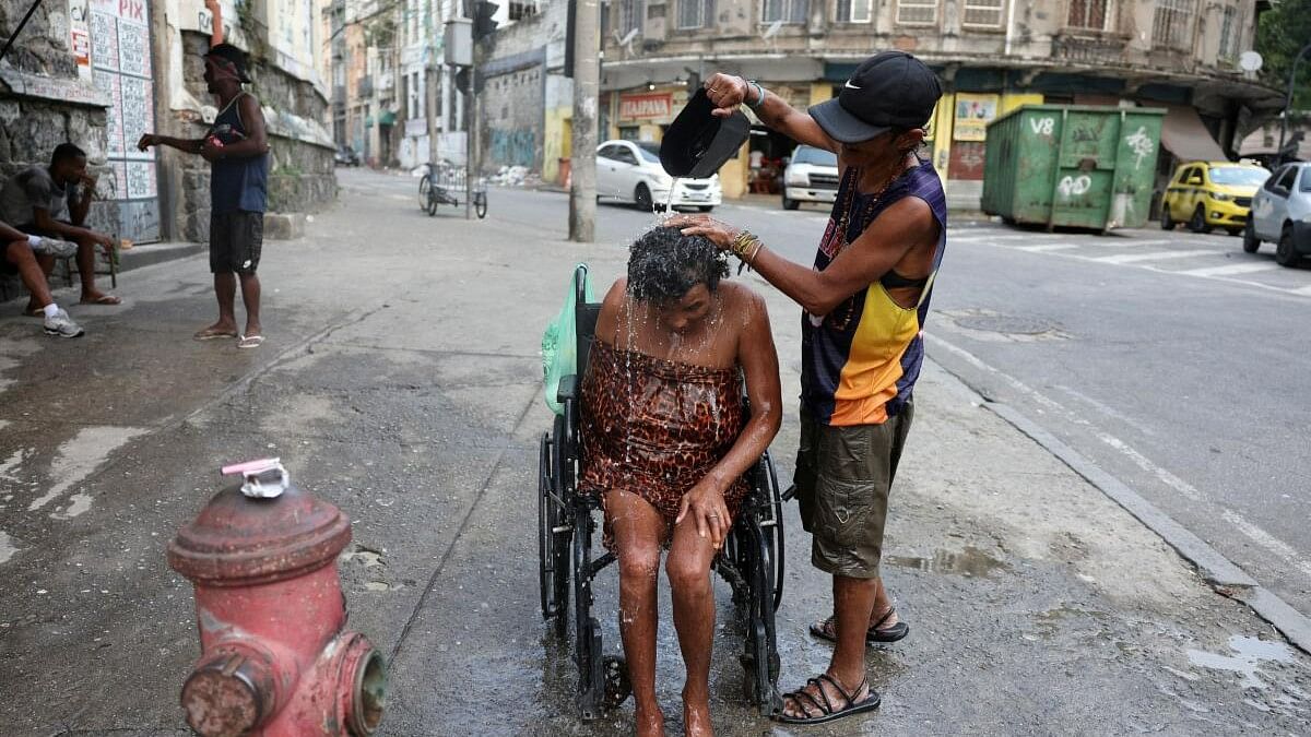 A woman throws water to a handicapped person to cool down amid a heatwave, on the street in Rio de Janeiro, Brazil November 18, 2023. 