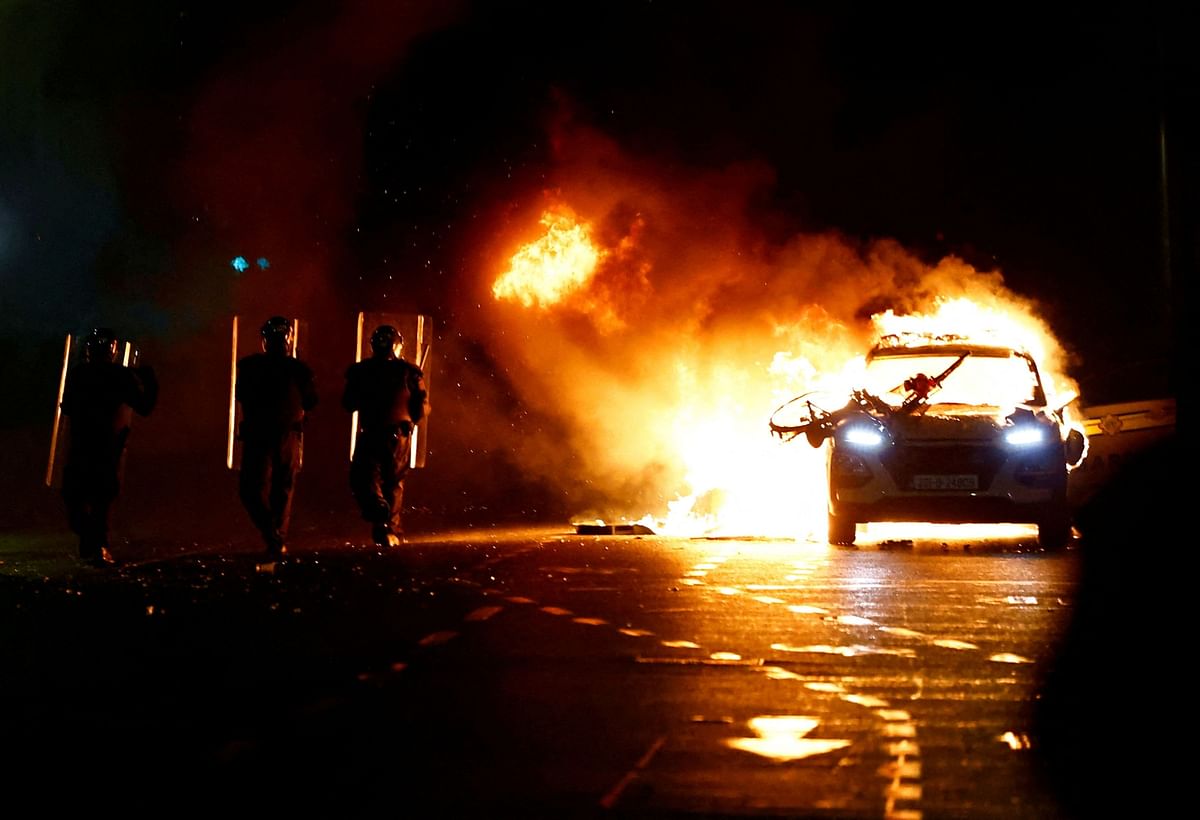 Riot police walks next to a burning police vehicle, near the scene of a suspected stabbing that left few children injured in Dublin, Ireland, November 23, 2023. 