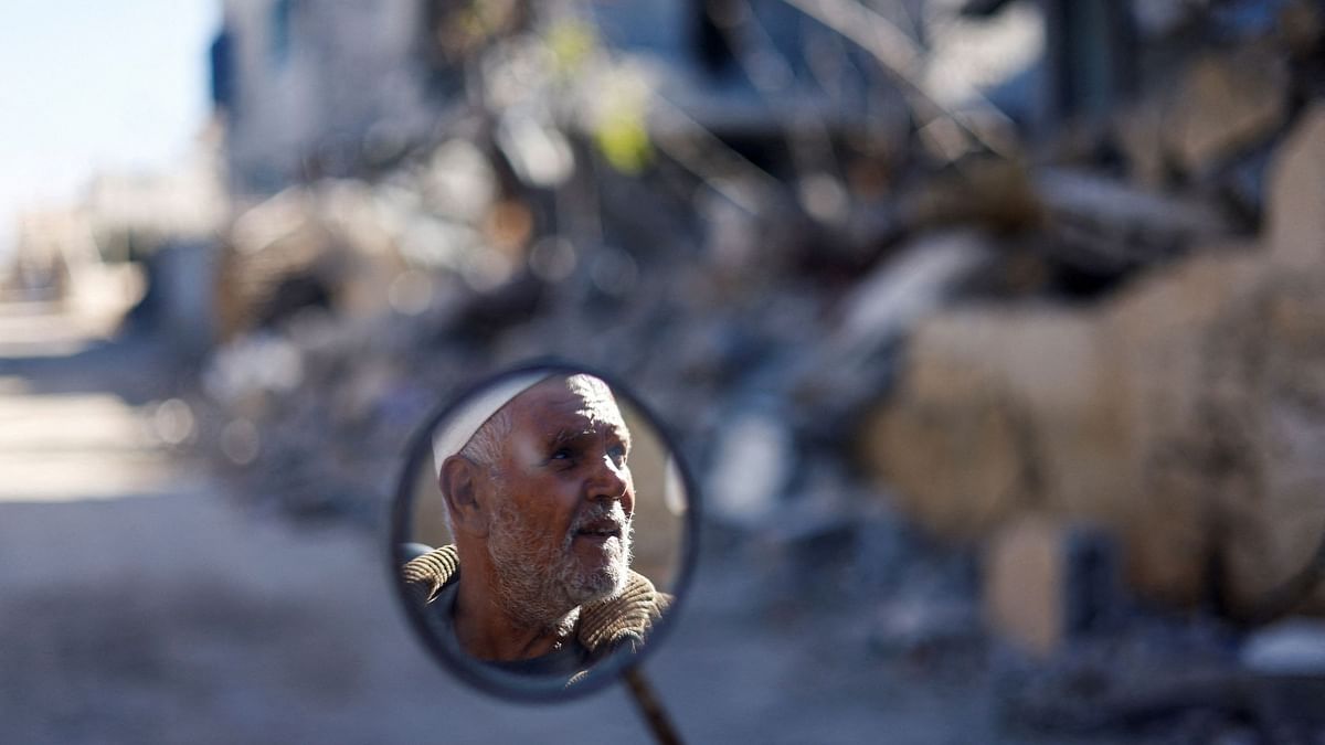 A man's face is reflected in a mirror, near the ruins of houses destroyed in Israeli strikes during the conflict, during a temporary truce between Hamas and Israel, in Khan Younis in the southern Gaza Strip. 