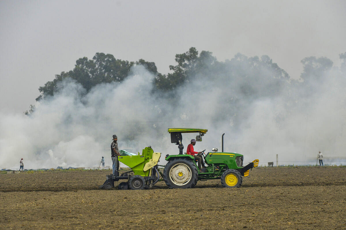 Farmers work on field as others burn paddy stubble, on the outskirts of Jalandhar.