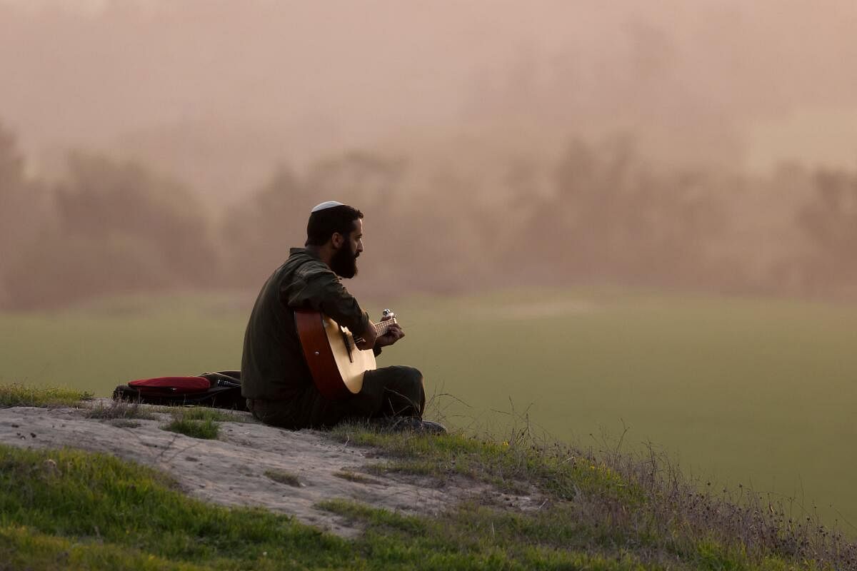 An Israeli soldier plays the guitar on a hill near the Israel-Gaza border, amid the ongoing conflict between Israel and the Palestinian Islamist group Hamas, in southern Israel, December 27, 2023. 