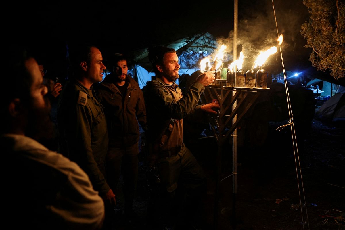Israeli soldiers light candles of a Hanukkiyah, a candlestick with nine branches that is lit to mark the Jewish holiday of Hanukkah, amid the ongoing conflict between Israel and the Palestinian Islamist group Hamas, near Israel's border with Gaza in southern Israel.