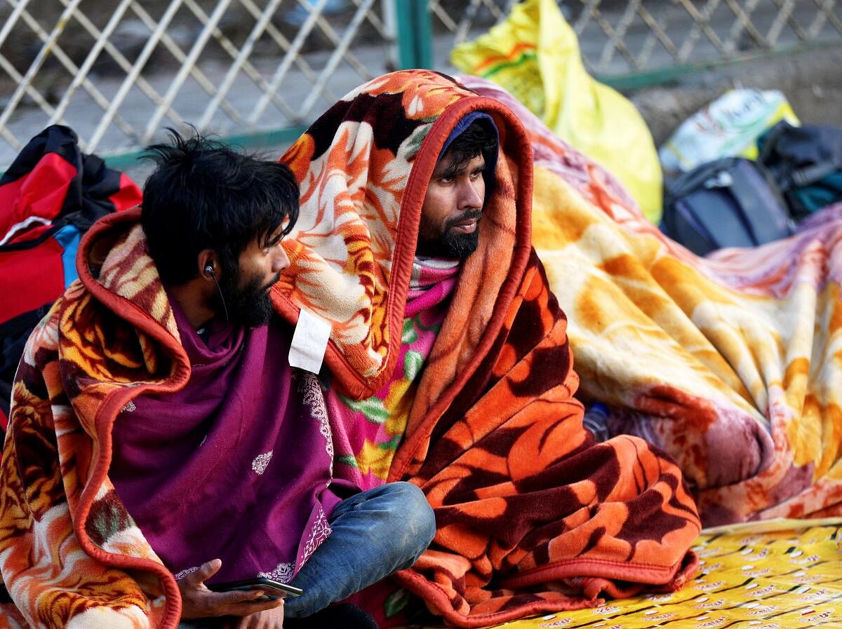 Passengers, wrapped in blankets, sit outside the Jammu railway station during a cold winter morning, in Jammu, Wednesday.
