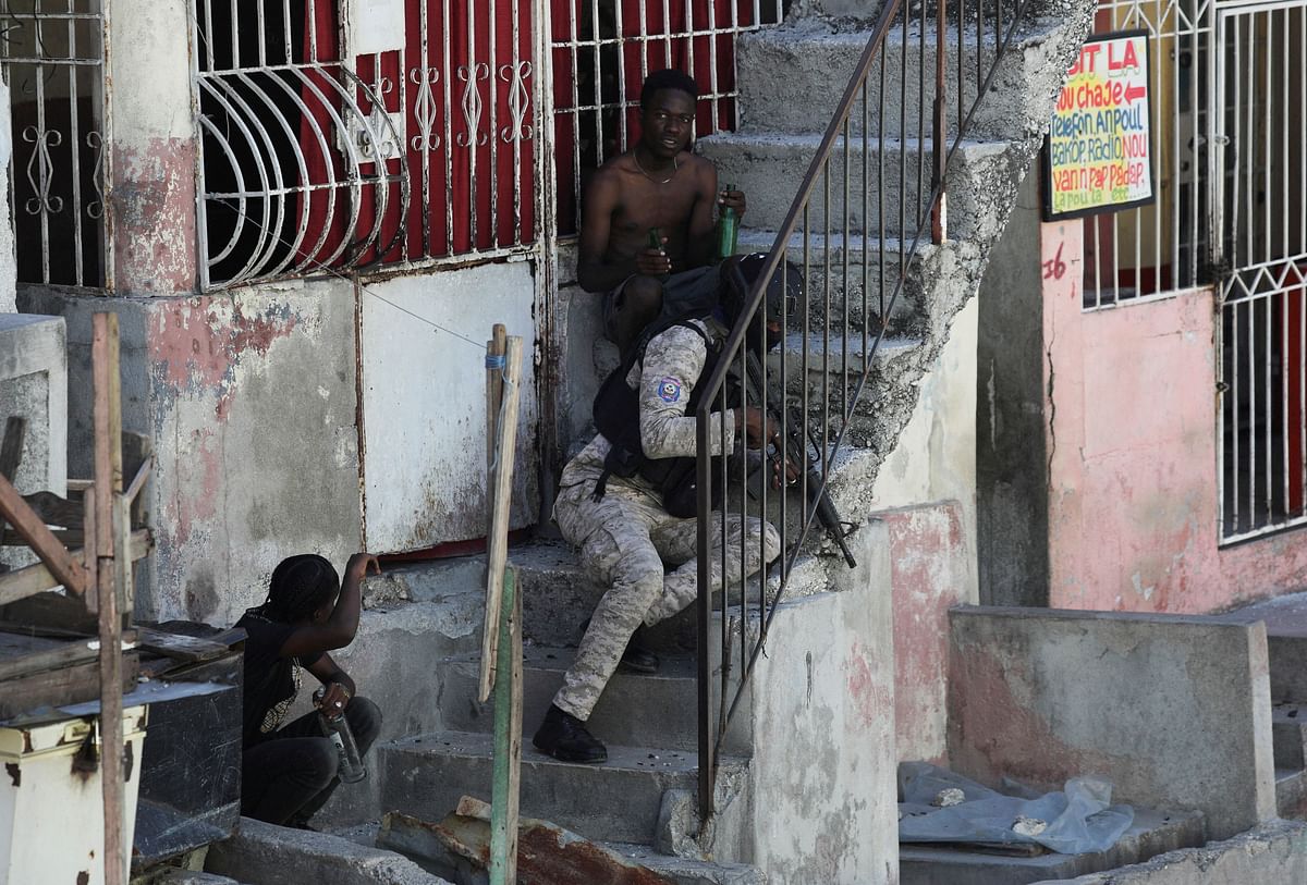 A police officer takes cover on a staircase next to civilians, as burning barricades across several neighbourhoods forced residents to take shelter, in Port-au-Prince, Haiti.