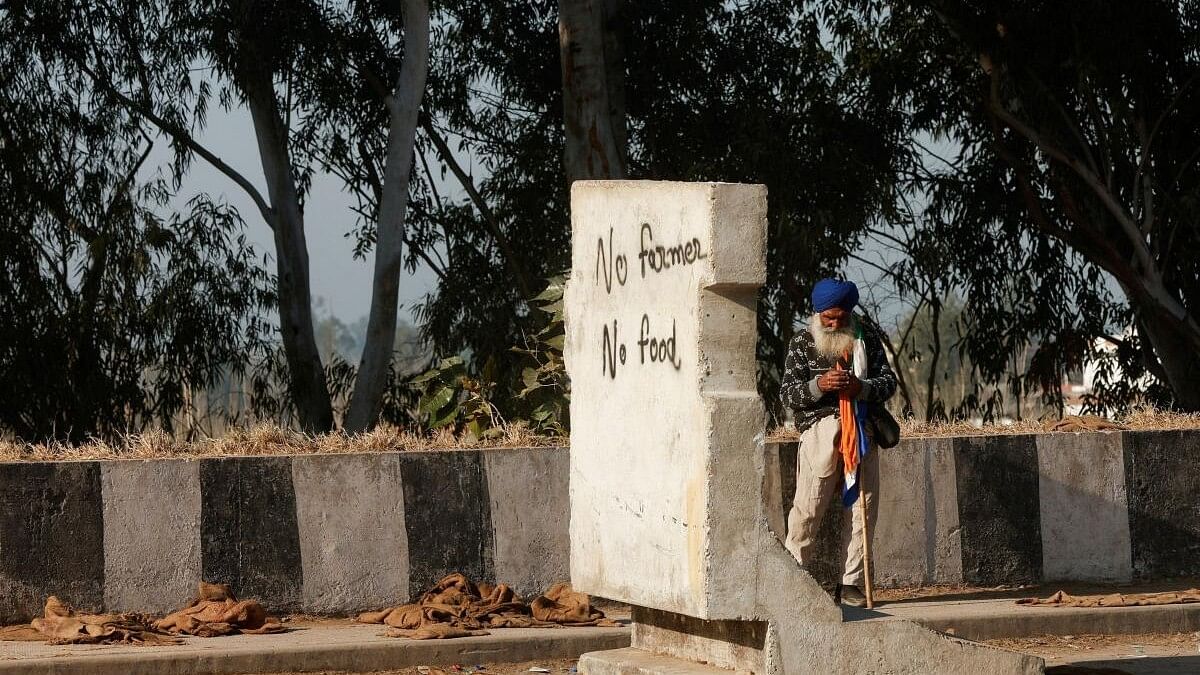 A farmer stands next to a concrete block at the site of a protest as they march towards New Delhi to push for better crop prices promised to them in 2021, at Shambhu Barrier.