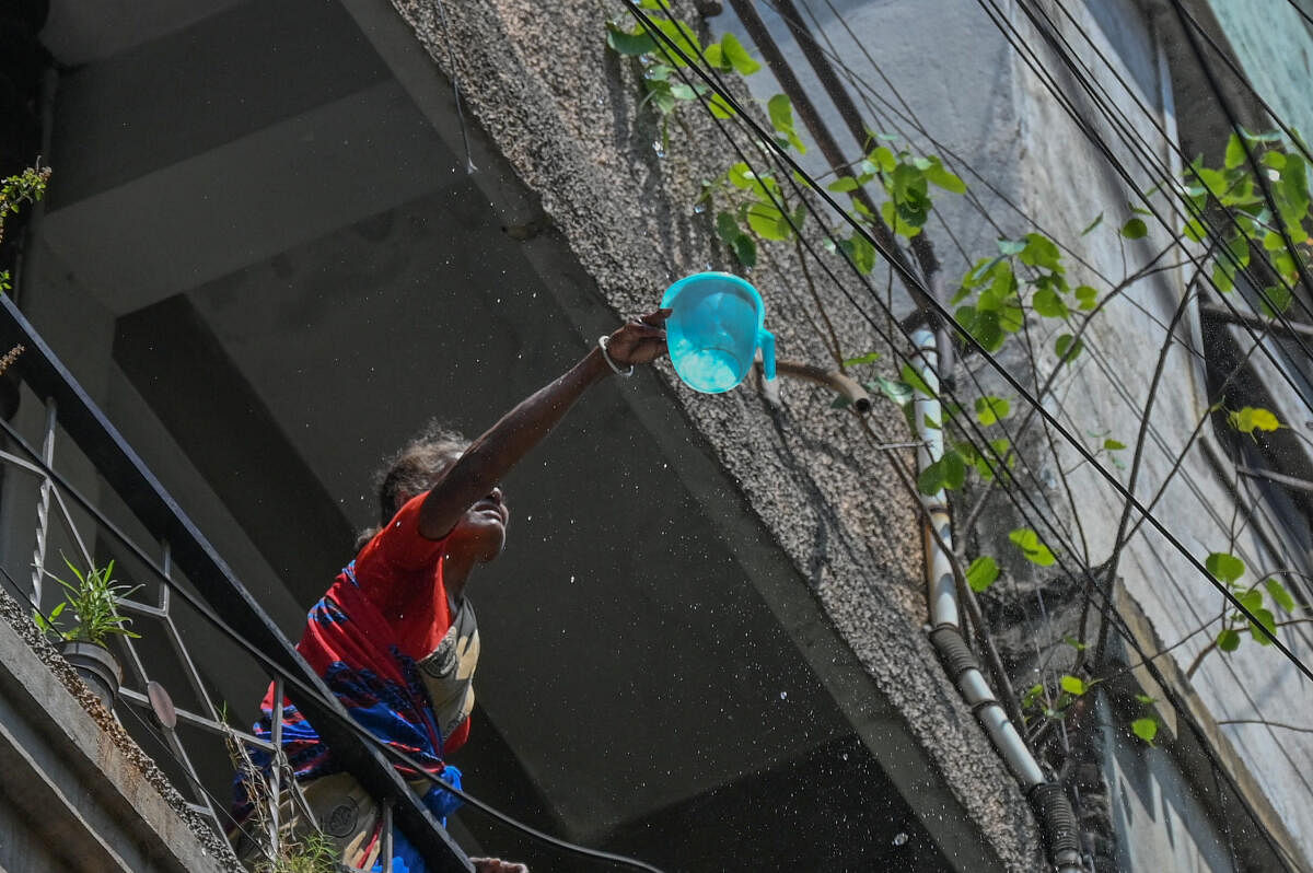 A woman tries to catch a stream of water falling from overhead tank at Sampagi Rama Nagar in Bengaluru.