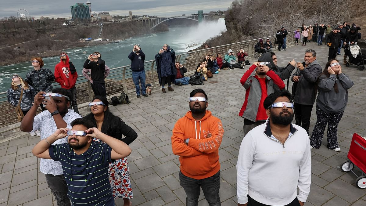 At Niagara Falls, New York, people look to the sky as the moon partially eclipses the sun.