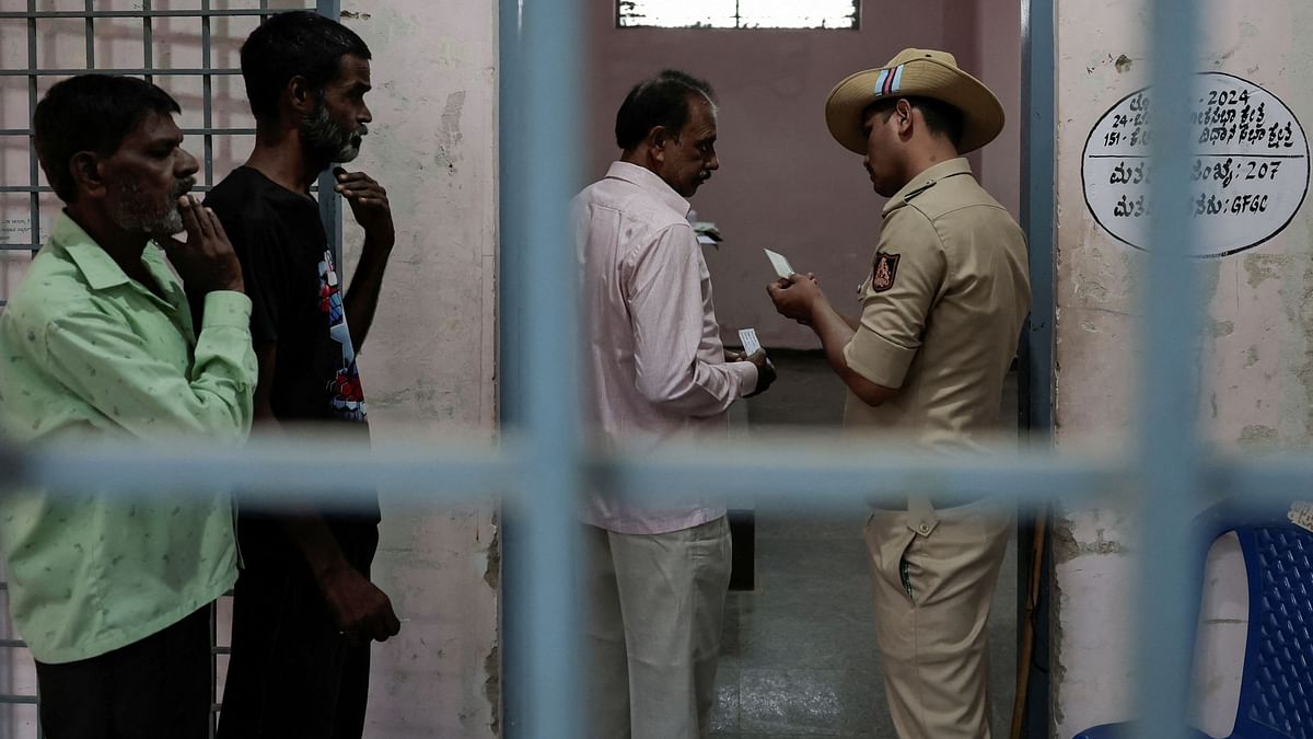A police officer checks the ID card of a voter before he casts his vote at a polling station during the second phase of the general elections, in Bengaluru.