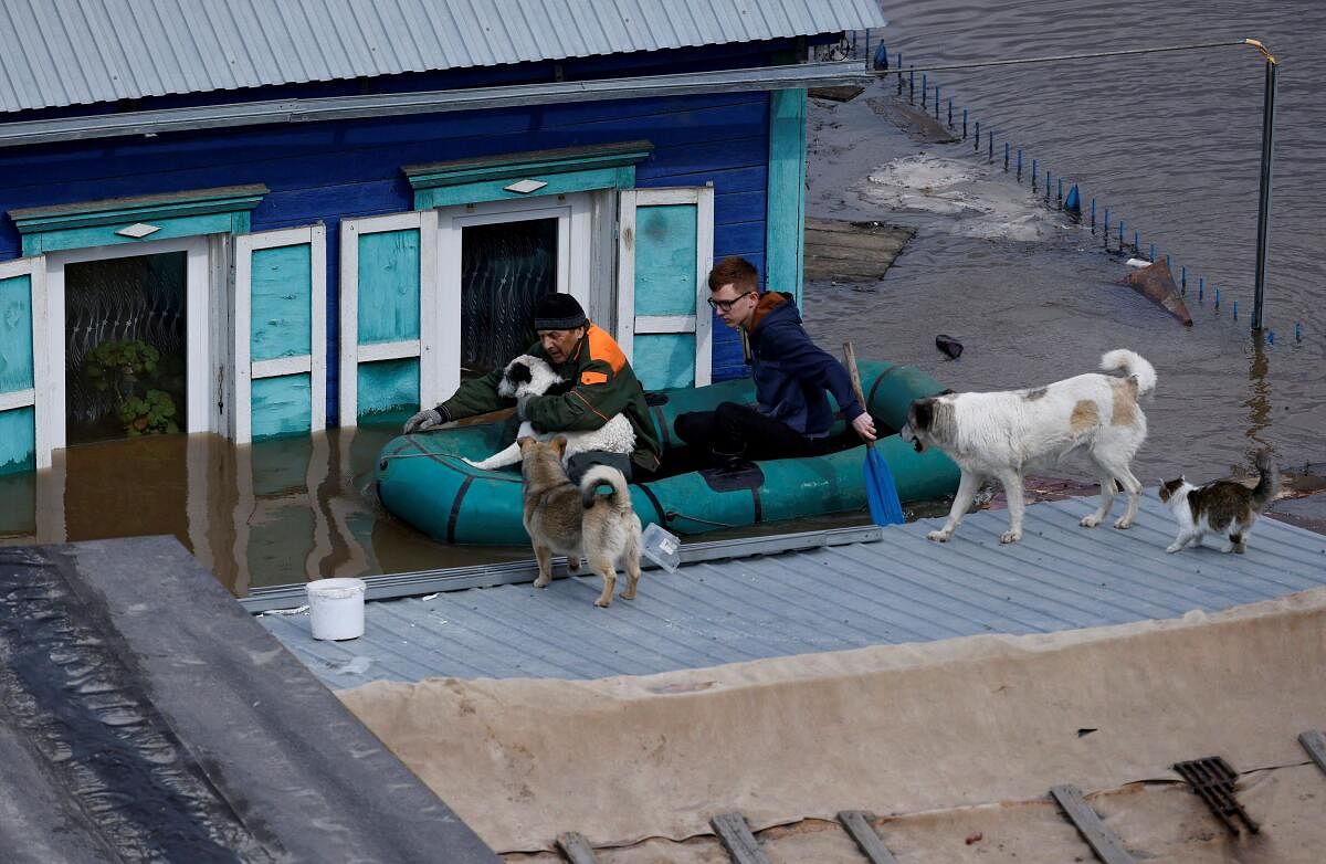 Local resident Alexander Timofeyevich (L) sails with a neighbour on an inflatable boat through the flooded yard of his house to feed the dogs stranded on the roof, in Orenburg, Russia, April 12, 2024. 