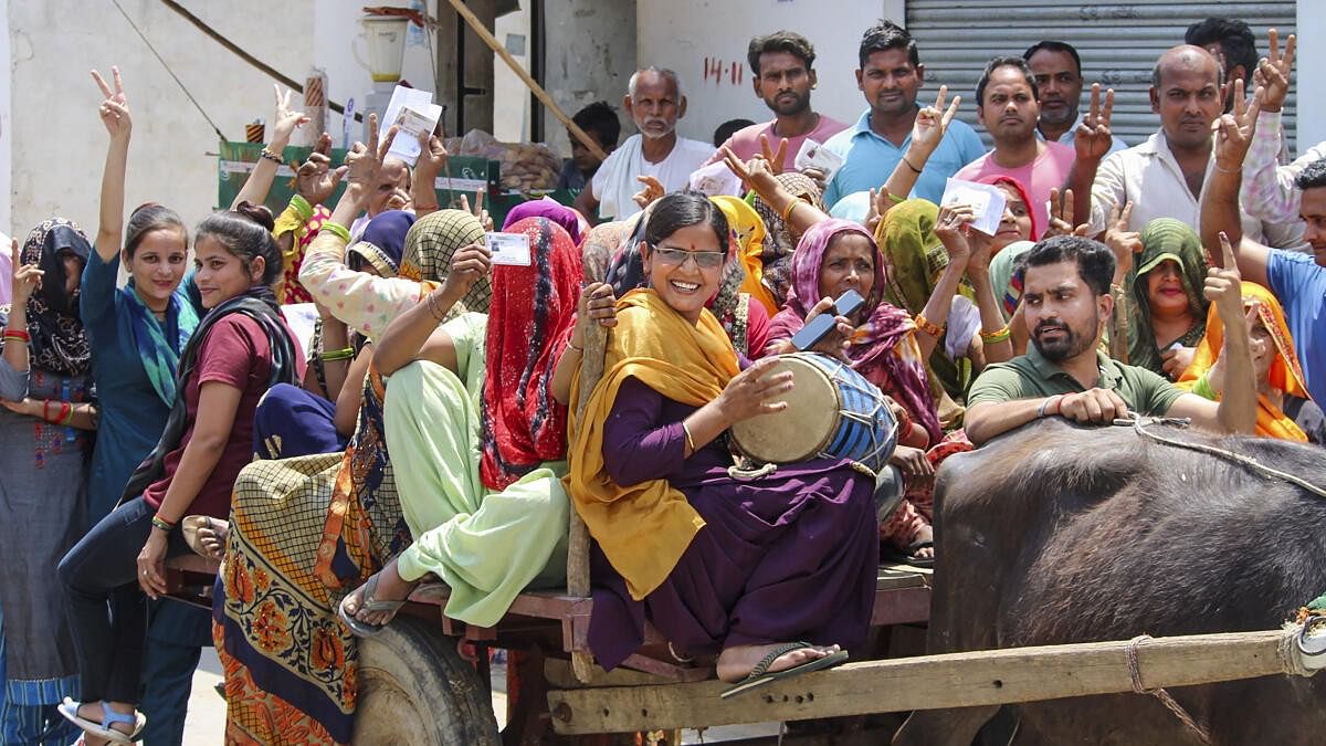 Women voters play a 'dholak' as they go to cast their votes on a bullock cart, for the second phase of Lok Sabha elections, in Bulandshahr.