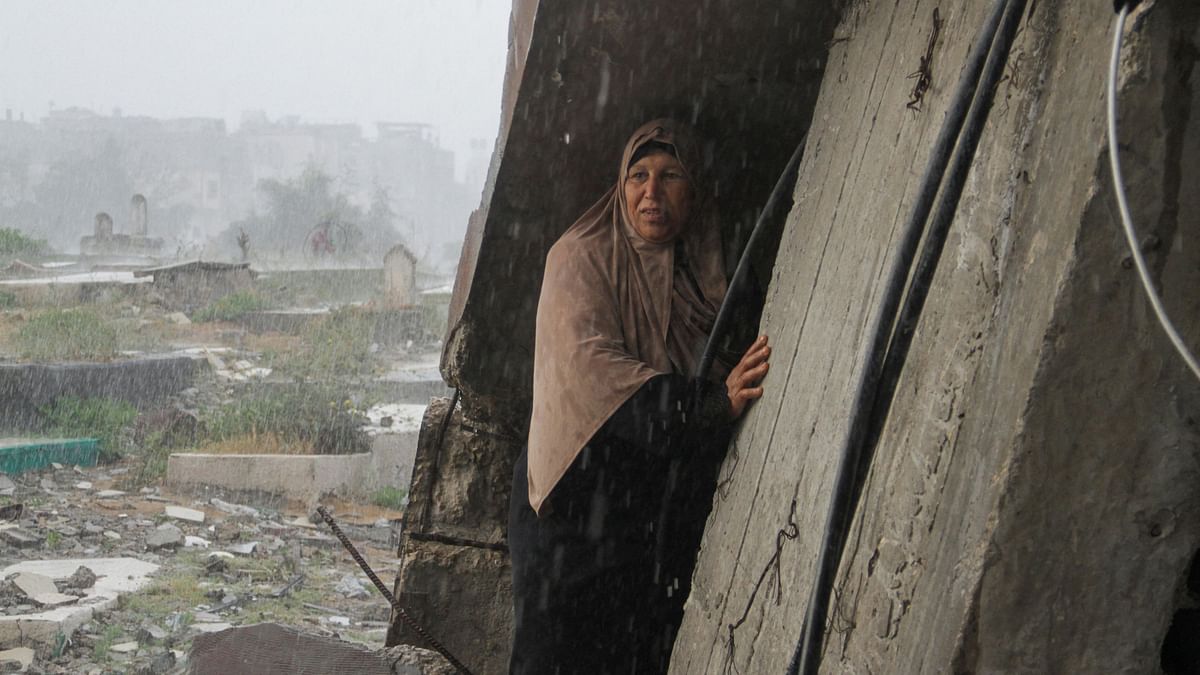 A woman takes shelter from the rain as she visit the grave on the day of Eid al-Fitr, in Gaza Strip.
