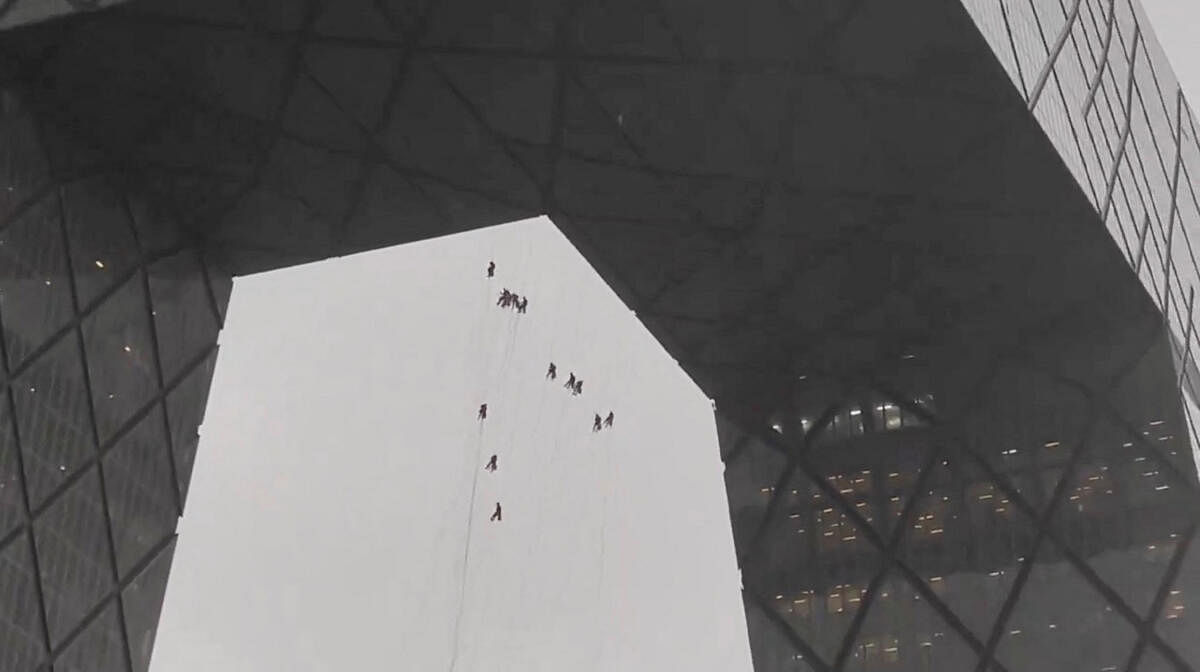 Workers hang from a building amid strong winds in Beijing, China in this screen grab obtained from a social media video.