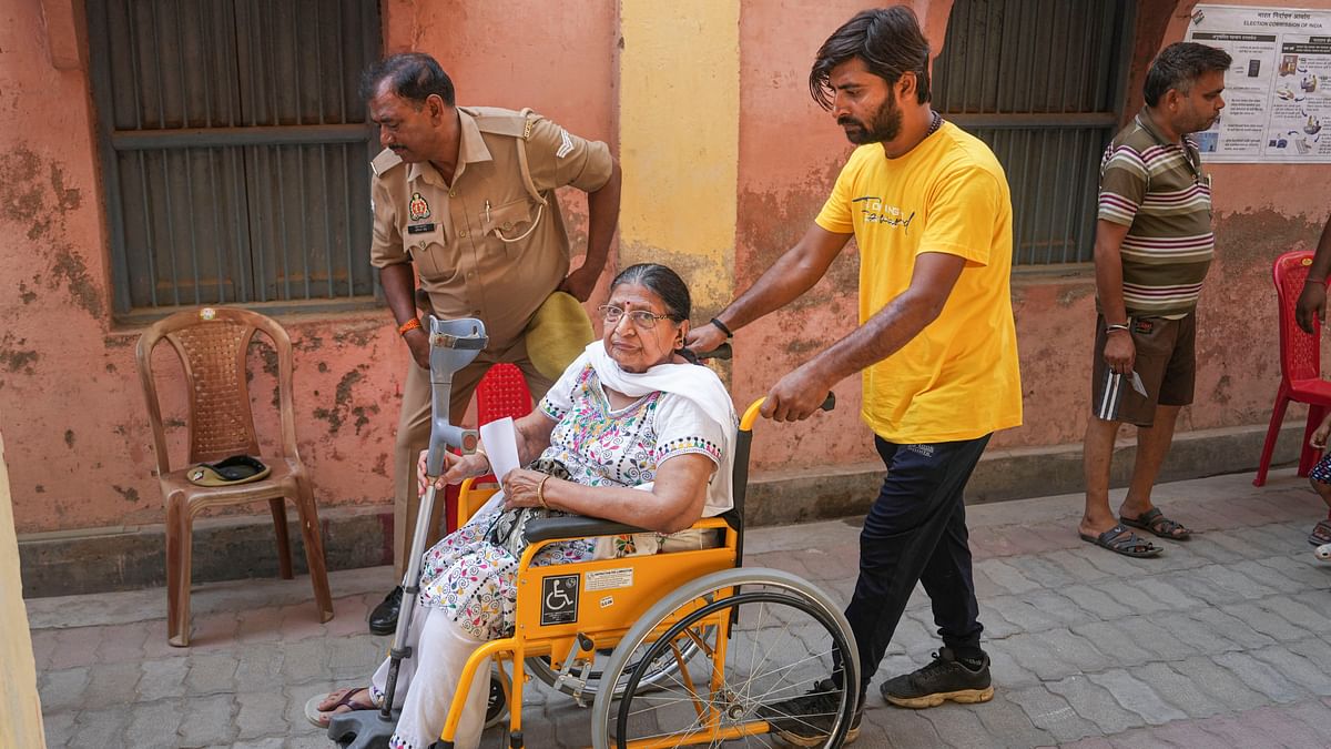 A woman with disability  being assisted as she arrives to cast her vote during the fourth phase of Lok Sabha elections in Kanpur.