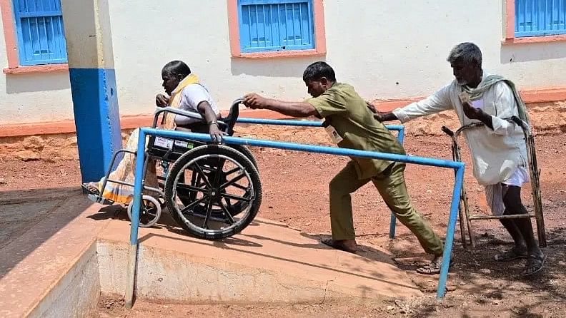 Renavva Jalapannavar (on the wheelchair) being helped to reach the polling station at the Government Higher Primary Boys' School at Kusugal village in Hubballi (Rural) taluk.