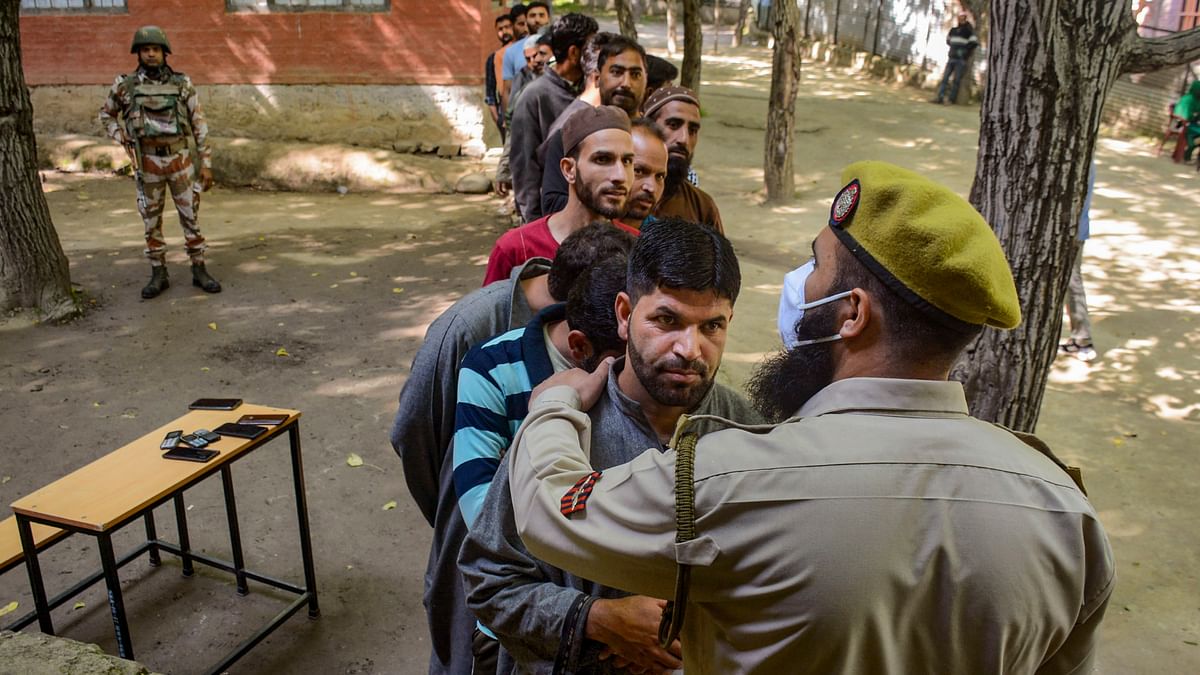 Security personnel stand guard as voters wait in a queue at a polling station to cast their votes for the fifth phase of Lok Sabha elections, in Budgam.