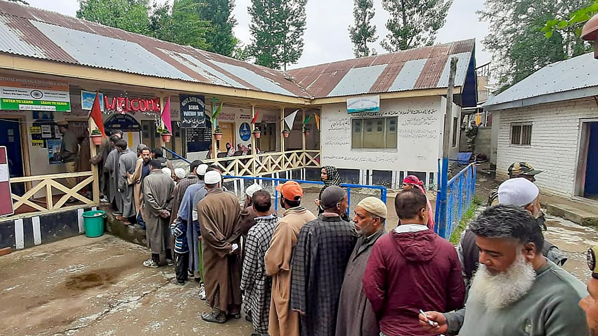 Security personnel stand guard as people wait in a queue to cast their votes at a polling booth during the fourth phase of General Elections 2024 in Srinagar, J&amp;K.