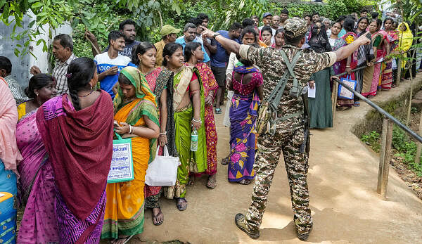 A security person guards as people wait in queues to cast their votes at a polling station during the sixth phase of Lok Sabha elections, in West Bengal's Purba Medinipur district.