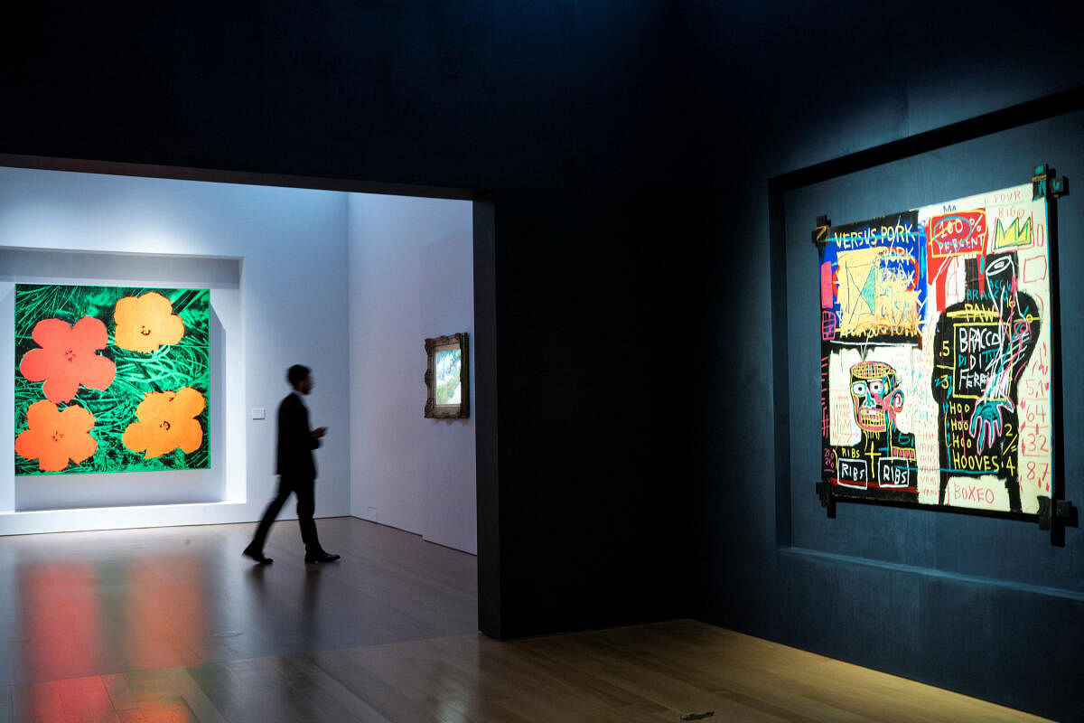 A man walks near Andy Warhol's "Flowers", Vincent Van Gogh's "Coin de jardin avec papillons" and Jean-Michel Basquiat's "The Italian Version of Popeye has no Pork in his Diet" during a media preview at Christie's