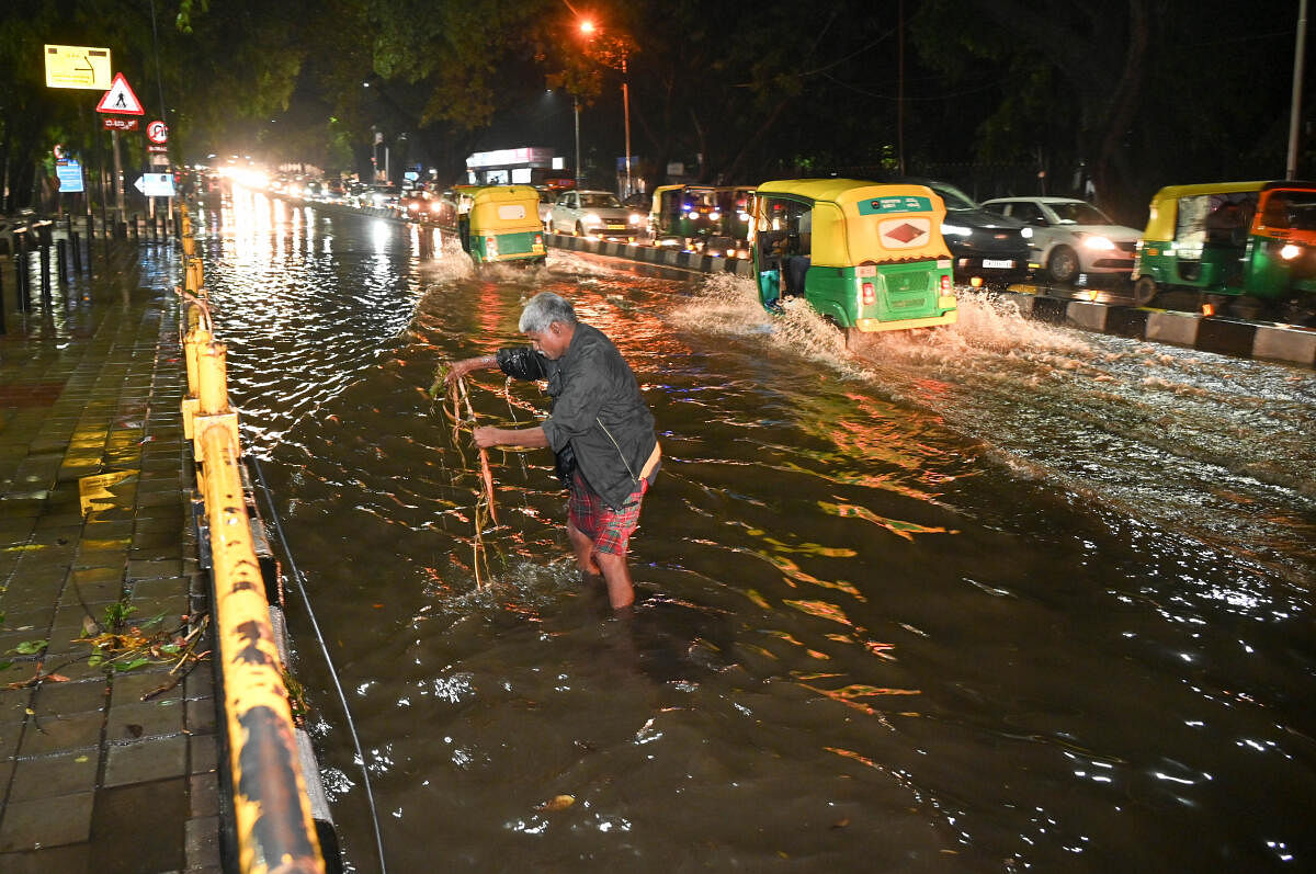 A man clears garbage which causing water loged drain, , during the heavy rain on Dr BR Ambedkar Veedhi, in Bengaluru.