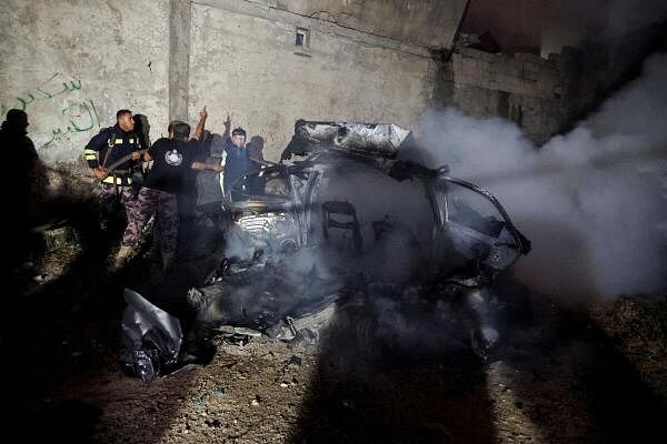 Palestinian Civil Defense members work at a destroyed vehicle in the aftermath of an Israeli raid, in Kafr Dan, near Jenin, in the Israeli-occupied West Bank.