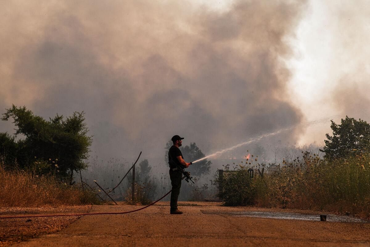 An Israeli security member sprays water on fire following rocket attacks from Lebanon.