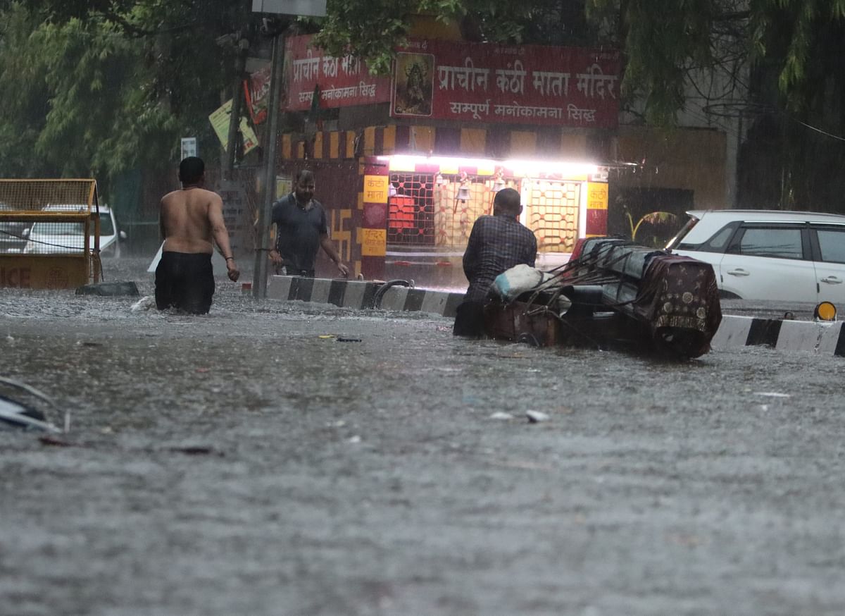 People wade through a waterlogged road amid rains, in New Delhi, Friday morning, June 28, 2024.
