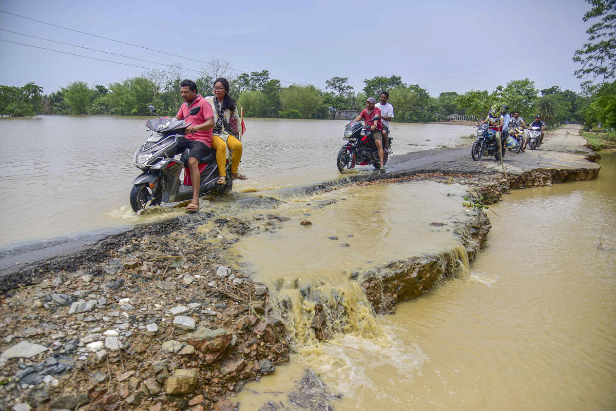 People ride two-wheelers on a road damaged by flood following rains in the aftermath of Cyclone Remal, in Nagaon district.
