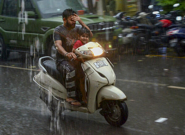 A man with a child rides a scooter during rains in Amritsar on July 10, 2024.