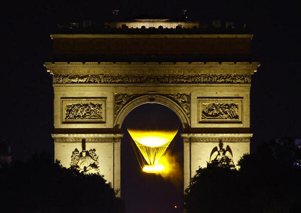 The Olympic cauldron and the Arc de Triomphe after sunset during the Olympics. 