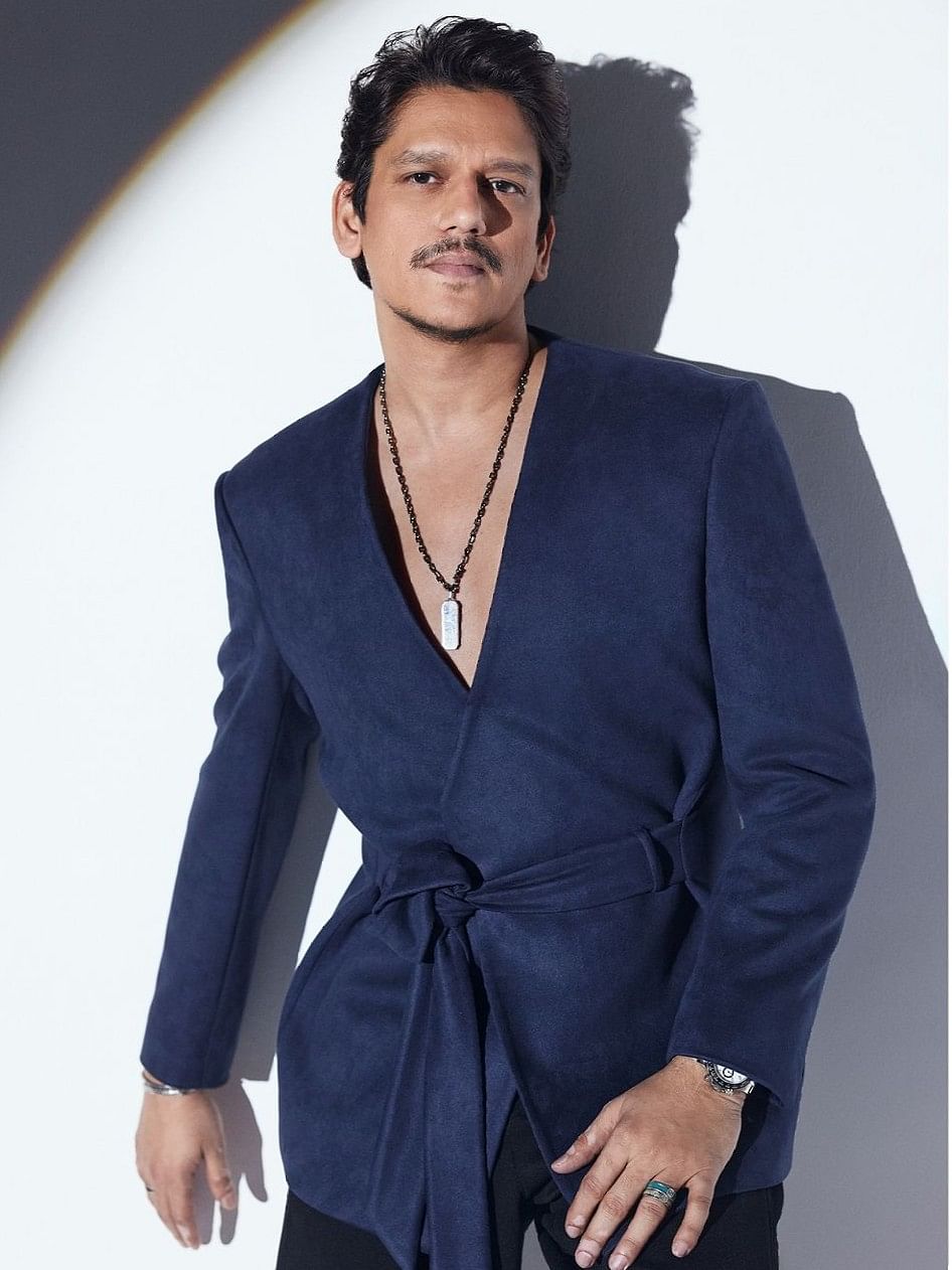 This navy blue suit stands out with its deep neckline and distinctive design that knots above the torso. Vijay Varma complements it flawlessly with a locket and chain, adding a touch of elegance and sophistication. The overall appearance is striking and innovative, making a bold fashion statement.