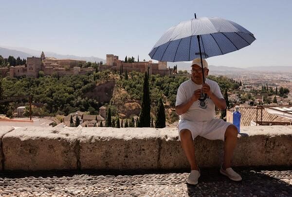 A tourist uses an umbrella at San Nicolas viewpoint in front of La Alhambra, during a hot summer day in Granada, Spain.