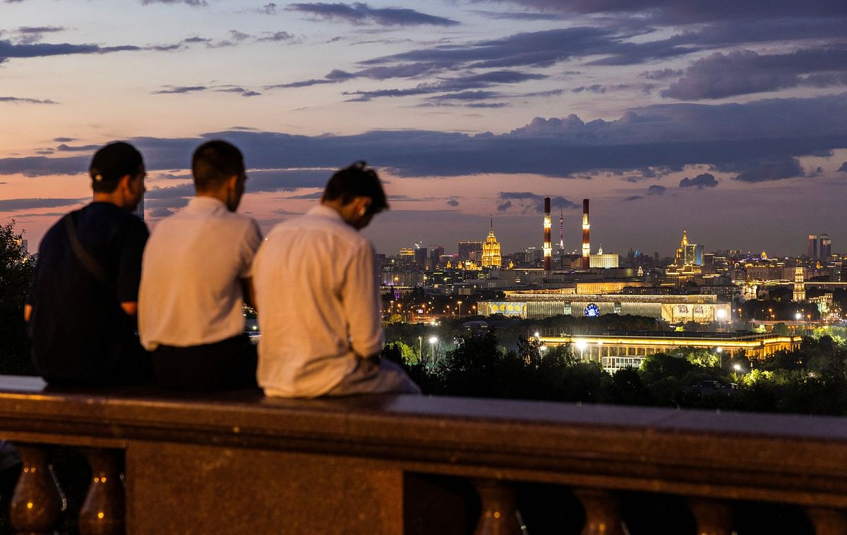 People sit on the parapet at Vorobyovy Gory viewpoint with the city’s skyline seen in the background in Moscow. 