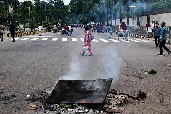 A pedestrian crosses a road near smoking objects during a protest demanding the stepping down of Bangladeshi Prime Minister Sheikh Hasina, following quota reform protests by students, in Dhaka, Bangladesh, August 4, 2024.