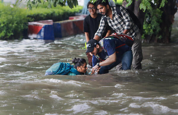 People help a pedestrian who fell on a flooded road after heavy monsoon rains at ITO in New Delhi.