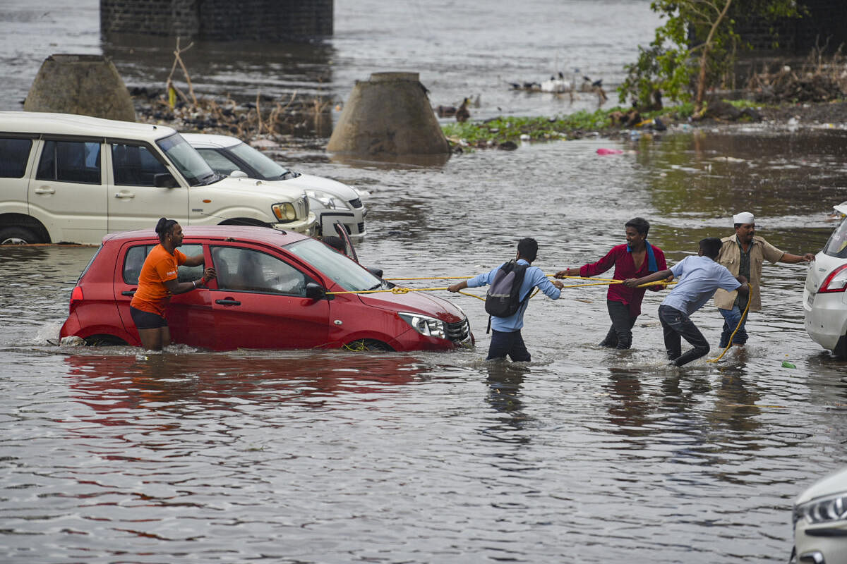 People try pulling out a car stuck in a waterlogged area after water released from the Khadakwasla Dam caused flood concerns following heavy rainfall, in Pune.