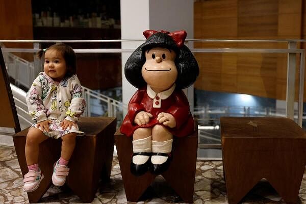 A girl named Anne Mai sits next to a sculpture of comic character Mafalda placed outside a bookstore in Sao Paulo.