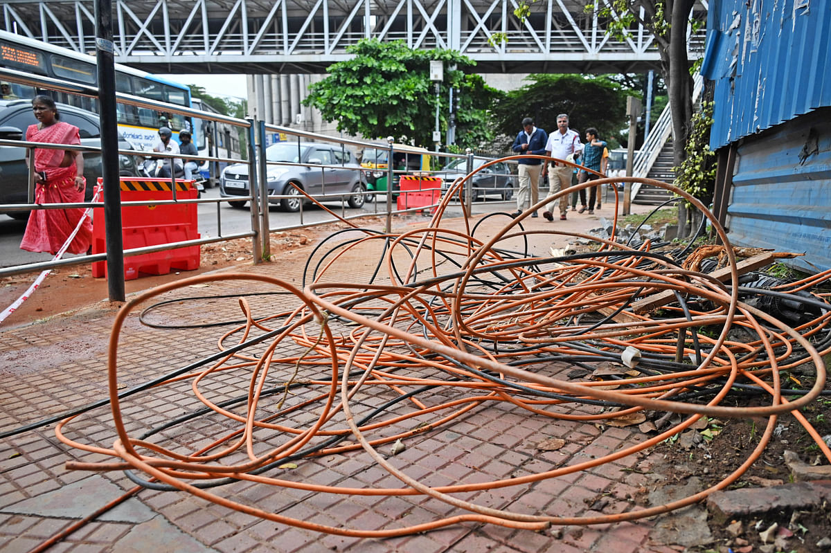 Pedestrians walk past bundled up optic fiber cables (OFC) occupying the footpath near Halasuru Gate Traffic Police Station Bengaluru on Sunday July 14 2024. 