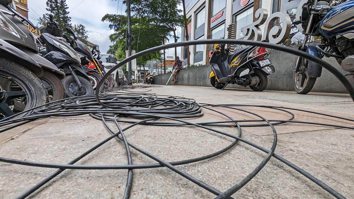 OFC cables dangle and vehicles occupy the footpath on Museum Road in Bengaluru on Wednesday. 