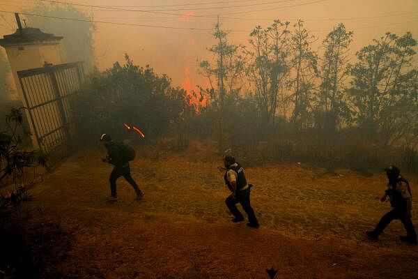 A person walks with a camera in hand along with two police officers through smoke from a burning wildfire, in Quito, Ecuador