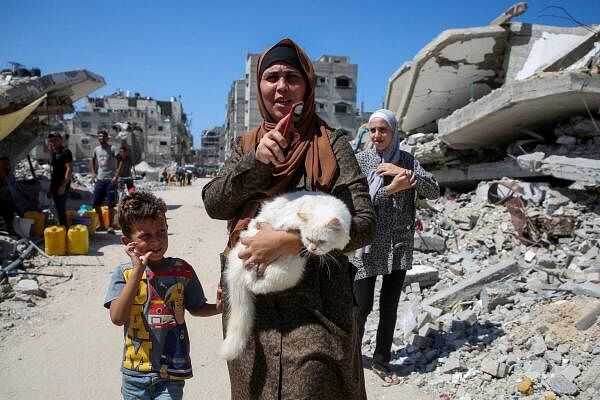 A Palestinian woman holds a cat as she walks past the rubble of houses destroyed in Israel's military offensive, amid the Israel-Hamas conflict, in Khan Younis, in the southern Gaza Strip.