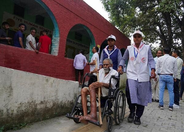 Volunteers assist a man in a wheelchair as he arrives at a polling station to cast his vote during the state assembly elections, in Karnal, Haryana.