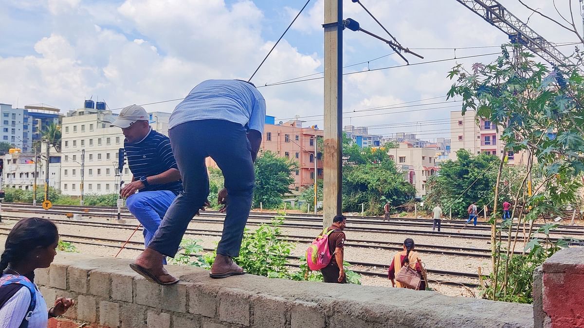 People jump over the railway station compound wall to cross the tracks to avoid the long walk. 