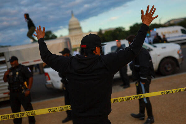 A demonstrator raises their arms as police officers stand guard during a protest in support of Native American tribes in front of the U.S. Capitol, in Washington.