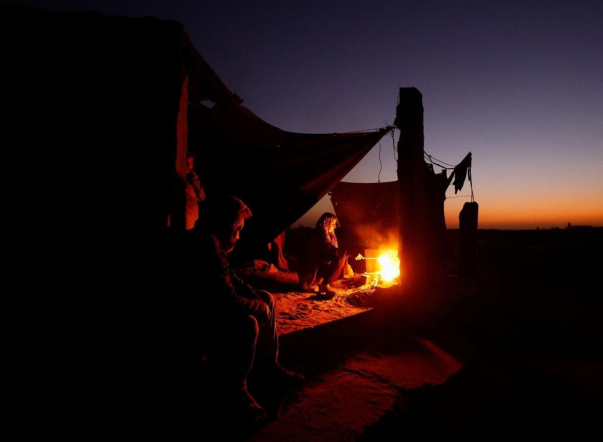 Displaced Palestinian light a fire next to their tent as they live at a cemetery in Khan Younis