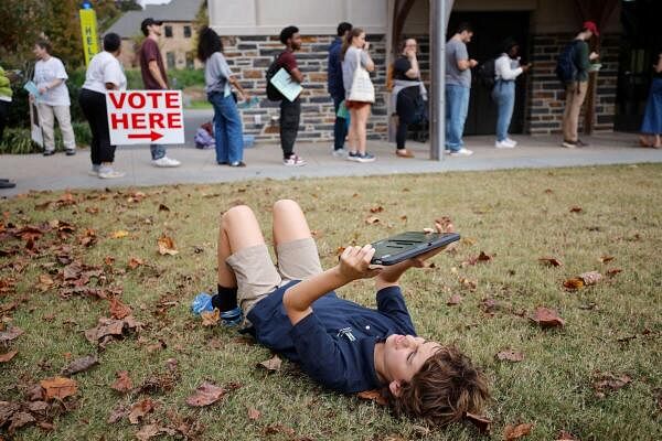 A young boy looks at his portable device while resting on the grass as his parents join a line of Duke University students and Durham County residents waiting to cast their ballots at a polling site on campus during the penultimate day of early voting in the state, in Durham, North Carolina, US.