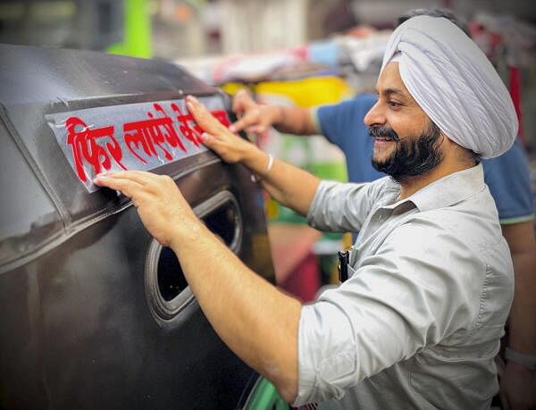 AAP leader Jarnail Singh pastes a banner on an auto-rickshaw at Tilak Nagar area, in New Delhi.