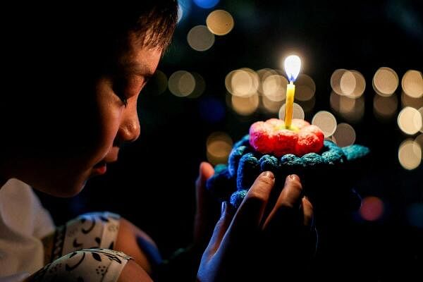 A boy prays before placing a Krathong, a floating basket made with leaves and flowers, into a park's lagoon during the Loy Krathong festival, held as a symbolic apology and to express gratitude to the goddess of the river for the water, in Bangkok, Thailand, November 15, 2024.