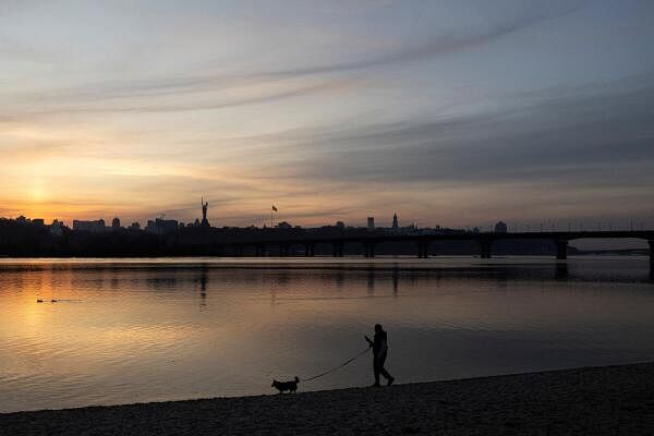 A woman with a dog walks along a bank of the Dnipro river during sunset, amid Russia's attack on Ukraine, in Kyiv, Ukraine.