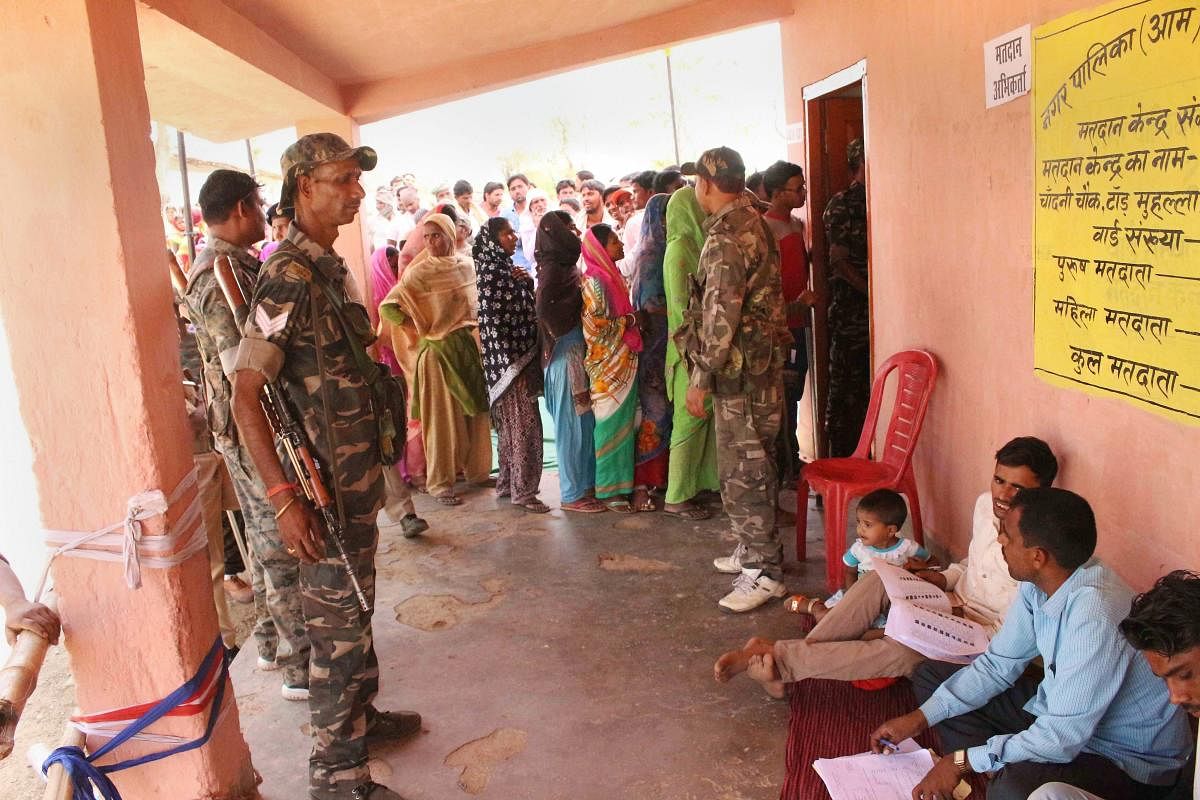 Security personnel guard as people queue up to cast their votes for panchayat elections in Latehar, Jharkhand, on Monday. PTI